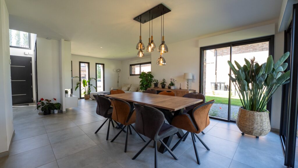 Pièce de vie ouverte avec table à manger, suspensions et grande baie vitrée donnant sur le jardin